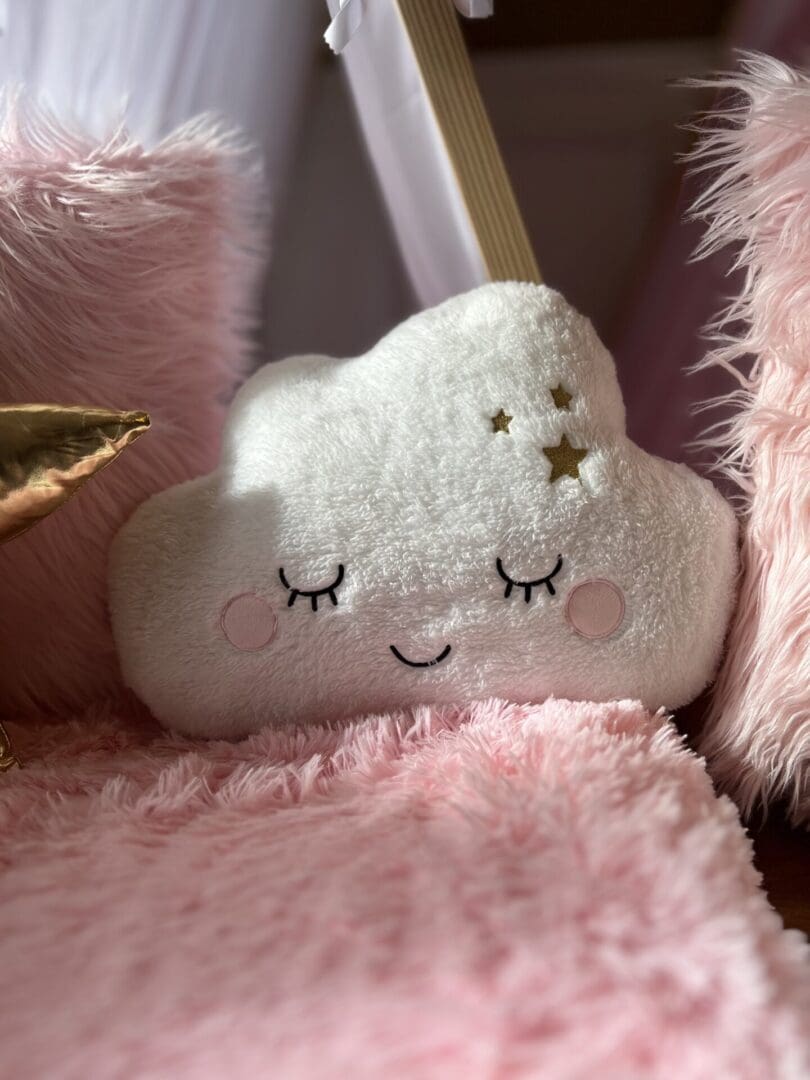 A cloud shaped stuffed animal on a pink blanket.