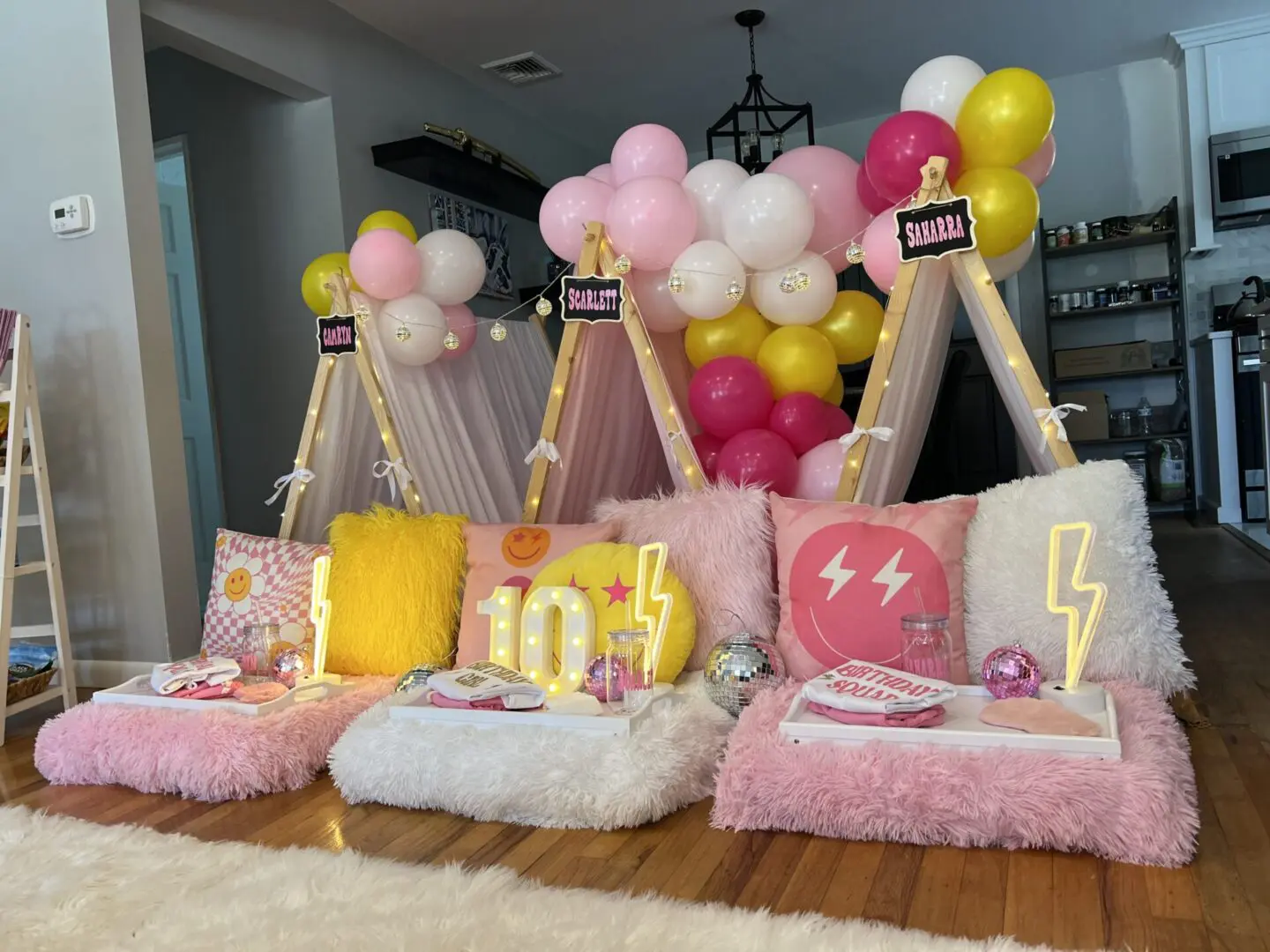 A pink and yellow teepee party with balloons and pillows.